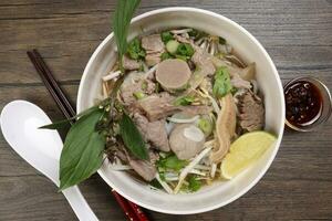 Vietnamese poh beef noodles soup broth with beef ball brisket tripe stomach parts been sprout thai basil lime in bowl on wooden table chopsticks spoon sauce photo