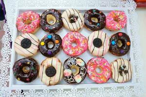 Donut variety on white tray outdoor daylight colourful sweet desert photo