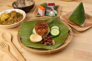 Nasi Lemak fragrant rice coconut milk with sambal friend peanut anchovy egg packed banana leaf round bamboo plate colorful nyonya kuih sweet desert palm leaf plate on wooden background photo