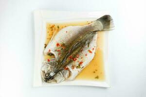 Thai style steam sea bass barramundi with lemon garlic chilli clear sauce on white serving dish photo