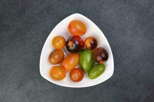 Red orange yellow green tomato mix variety on white triangle shape plate black slate background photo