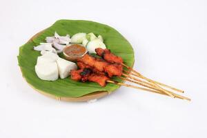 Chicken beef mutton meet Satay set nasi impit sticky rice cake sliced onion cucumber sweet peanut sauce on banana leaf bamboo basket on white background photo