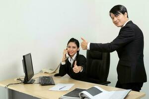 Young Asian male female wearing suit sitting at office desk telephone thumbs up photo