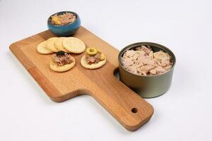 Tuna fish spread topping cracker biscuit tapas corn green black olive small bowl on wooden board tuna flake chunk in tin can over white background photo