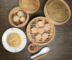 Prawn shrimp shaomai Xiao long bao dim sum dumpling chicken prawn fish seafood vegetable in bamboo steamer fried rice on plate sauce chopsticks soup spoon over rustic background photo