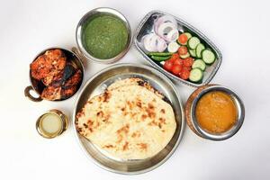 Spicy red Chicken grilled tikka tandoori nan bread green spinach curry yogurt sauce dal tomato cucumber onion salad set in metal stainless steel brass copper pot on white background photo