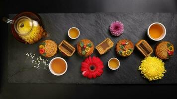 Colourful flower decorated mooncake Chinese mid autumn festival on black slate stone background small white ceramic teacup glass teapot daisy chrysanthemum mum rose flower red yellow pink violet photo