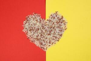 Mixed low glycaemic index healthy rice grain basmati millet buckwheat red rice hart shape on red yellow background photo