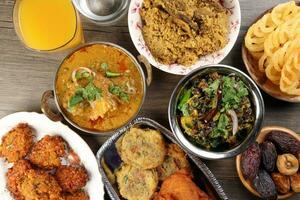 Bengali Iftar Ramadan breakfast spread ripe dates peep fried spicy piaju onion fitter eggplant tanpura potato chop haleem jilapi khichuri rice chana sola curry on rustic wooden table photo