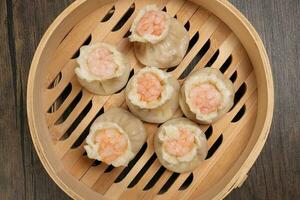 Prawn shrimp shaomai dim sum dumpling in bamboo steamer on rustic wood background photo