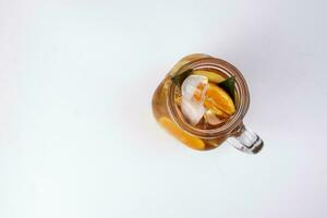 Liquid ice lemon orange tea with slice green leaf cinnamon stick in transparent glass jar mug on white background top view photo