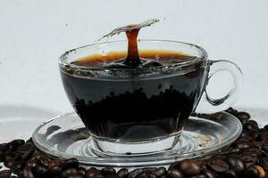 Coffee splash pillar in transparent glass cup saucer full of liquid coffee on coffee been bed white background photo