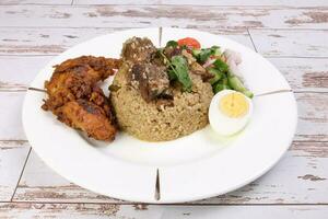 Beef Biryani Tehari with boiled egg coriander leaf garnish chicken curry pot roasted leg tomato cucumber onion chili coriander salad on white plate set over rustic wood background photo
