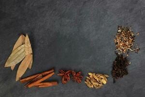 Mix variety spice cinnamon cardamom clove bay leaf wooden border frame copy text space on black slate background photo