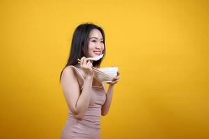 Beautiful young south east Asian woman holding chines empty chopstick Chinese soup spoon bowl utensil pretend acting posing see eat taste smell feed offer satisfaction yummy yellow orange background photo