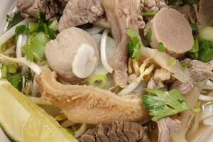 Vietnamese poh beef noodles soup broth with beef ball brisket tripe stomach parts been sprout thai basil lime in bowl on wooden table photo