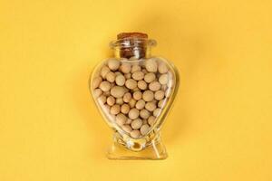hart shape glass bottle filled with soya beans on yellow background photo