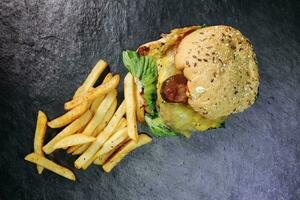 Gourmet beef burger multigrain bun with potato fries on black slate stone background top view photo