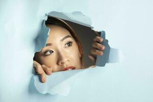 Young beautiful Asian woman expression through torn paper hole photo