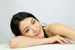 Young beautiful Southeast Asian woman beauty fashion makeup light grey white background laying on her hand smile at camera photo