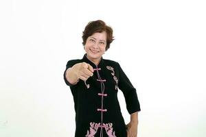 Elderly asian Chinese female wearing black tang samfu on white background happy smile point finger at camera photo