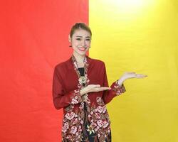 Asian woman traditional maroon kebaya sharong on red yellow paper background posing show display palm of hand photo