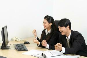 young Asian male female wearing suit sitting at office desk show point computer monitor happy success photo