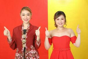 Two Asian woman traditional kebaya and modern dress red yellow paper background thumbs up photo