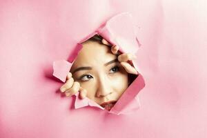 Young beautiful Asian woman expression through torn paper hole photo