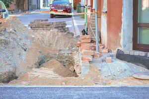 The road repair and caution with red bricks stacked near the hole in the road and lots of sand photo