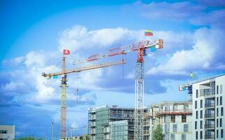 Construction site with cranes with flags Lithuanian and Lithuanian coat of arms building residential buildings on blue sky background with fluffy white clouds photo