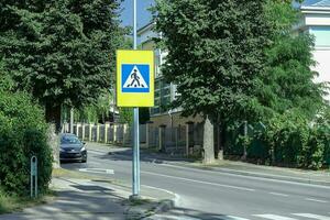 Blue road crossing sign in broght yellow green shield near zebra crossing in residential area in a city with green trees photo