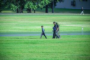 familia con un chico niño caminando en un camino Entre verde césped céspedes en soleado día foto