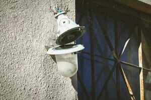 A broken white street lamp with coweb hanging on the wall near dark window photo