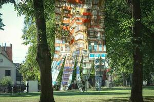 Low angle view of residential yellow brick building reflection in mirror design art object in city square greenery and sunlight photo