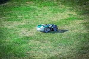 Small green robot lawn mower on a large green grass field on sunny day photo