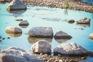 Close up of rocks on the river bank near blue water puddle on sunny day photo