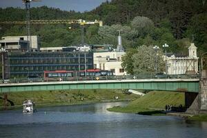 Vilnius, Lithuania 03 06 2022 Old buildings in greenery of Vilnius city center and red bus on a Green Bridge over the Neris river photo