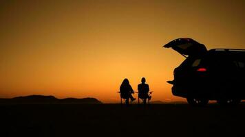 casal desfrutando cênico pôr do sol em uma Califórnia deserto assentos Próximo para seus veículo video