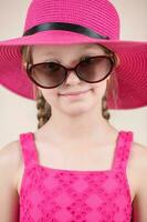 pequeño niña con rosado vestir sombrero y Gafas de sol foto