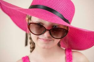 pequeño niña con rosado vestir sombrero y Gafas de sol foto