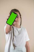 Young girl showing smartphone with green screen isolated on beige background photo