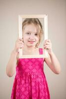 retrato de un linda pequeño niña participación un imagen marco. estudio Disparo foto