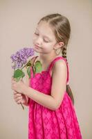 pequeño niña en un rosado vestir con un ramo de flores de lilas foto