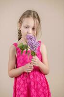 pequeño niña en un rosado vestir con un ramo de flores de lilas foto