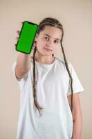 Young girl showing smartphone with green screen isolated on beige background photo