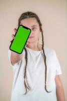 Young girl showing smartphone with green screen isolated on beige background photo