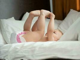 Baby with diaper lying on bed with legs raised up photo