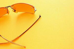 Old broken eyeglasses with damaged legs on orange background. Poor eyesight. Reuse and repair concept. Idea of health. Failure optic eyewear. Breakage of vision correction glasses. Close up, flat lay photo