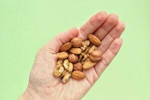 Almond, hazelnut, walnut  in the palm of outstretched hand on green background. Healthy eating diet, nutrition, vegan concept. Protein organic food. Dry snack. National nut day. Copy space for text photo
